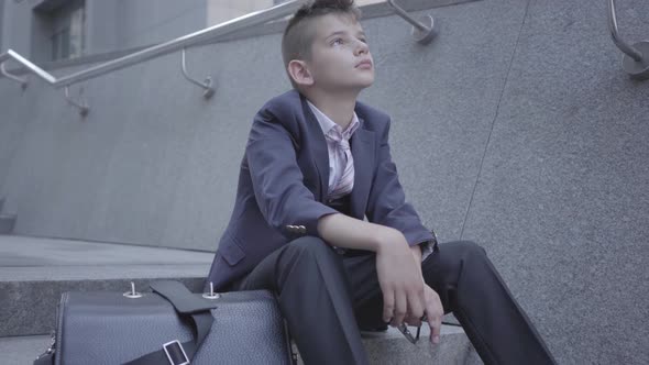 Sad Well-dressed Boy Sitting on the Stairs on the Street