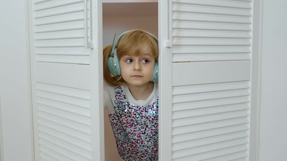 Little Child Girl Wearing Headphones Listening To Music and Funnily Dancing Near Wardrobe at Home