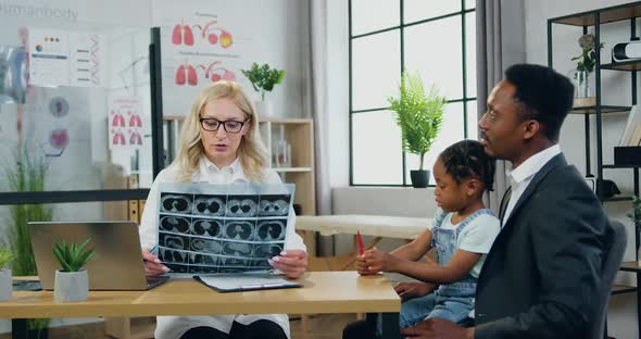 Female Doctor Explaining Girl's Brain X-ray Image to Handsome Serious Caring Black-Skinned father