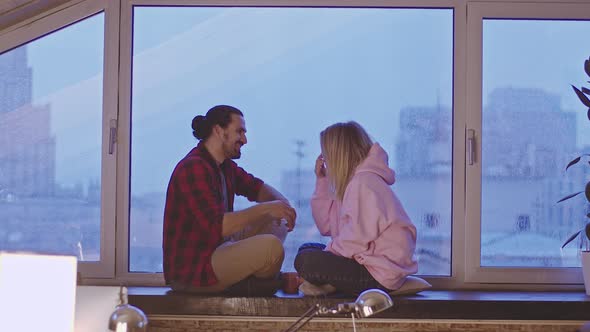 Young Heterosexual Couple Talking Cheerfully While Sitting By the Window