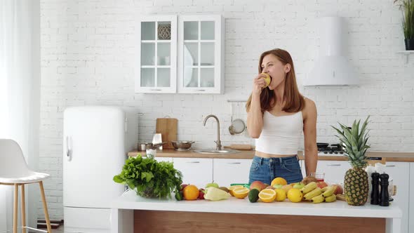 A beautiful sports girl at home in the kitchen eats a fresh apple.