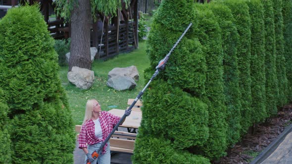 Blond Women Using Electric Trimmer for Cutting Hedge on Back Yard