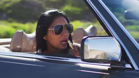 African american woman applying lipstick while looking in the mirror of convertible car