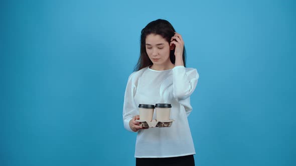 The Shy Young Woman with Two Glasses of Coffee in Her Hand Looks Blushing Ahead Puts Her Hair Behind