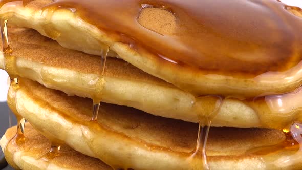 American pancakes with maple syrup on a white background. Pancake lies on a black slate round stone.