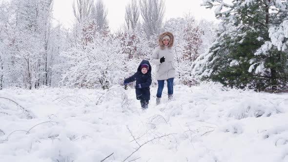 Mom and Son are Running in a Snowy Winter Forest Happy Parenthood and Family Vacation Slow Motion