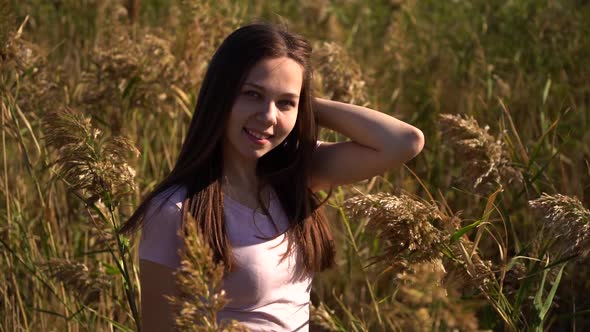 Attractive Portrait of Young Girl in Pink T-shirt in Field Looking in Camera. Out of Focus and Then