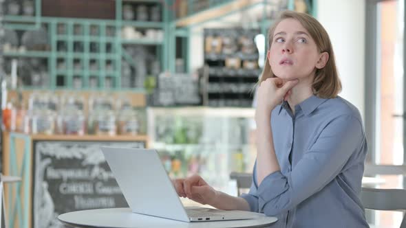 Young Woman Thinking While Using Laptop in Cafe