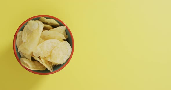 Close up of potato chips in a bowl with copy space on yellow surface