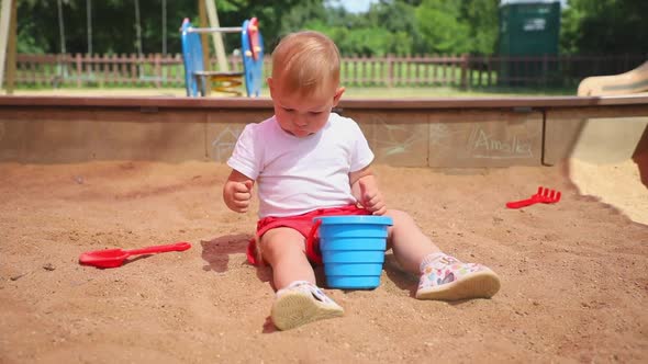 Adorable Toddler Girl Playing with Sand on Sandbox in Playground