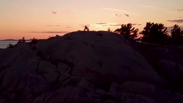 Inukshuk on Top of Rocky Pine Tree Island at Sunset, Drone Aerial Wide Orbit Pan. Reveal of Blue Lak