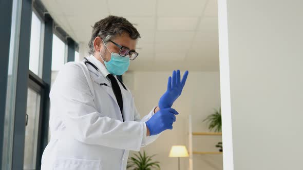 Senior Doctor in a Protective Mask Puts on Medical Gloves