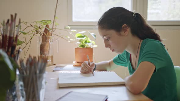 Teenage artist sitting drawing in a sketchbook in her room