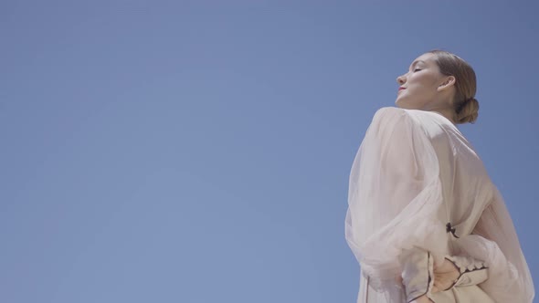 Beautiful woman in white dress on background of sky