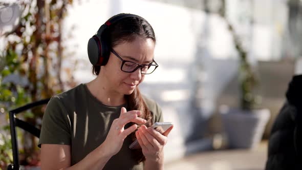 Adult Woman is Listening to Music By Headphones and Using Smartphone When Had Breakfast in Cafe