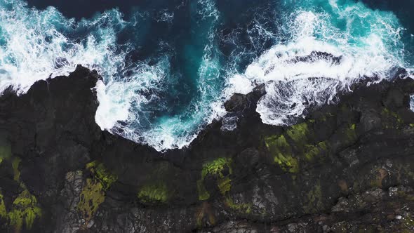 Aerial View of Waves Break on Rocks of Faroe Islands Cliffs in a Blue Ocean