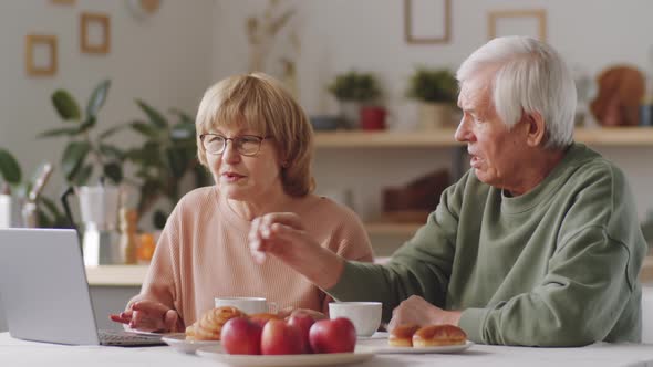 Senior Couple Using Laptop, Chatting and Embracing at Home