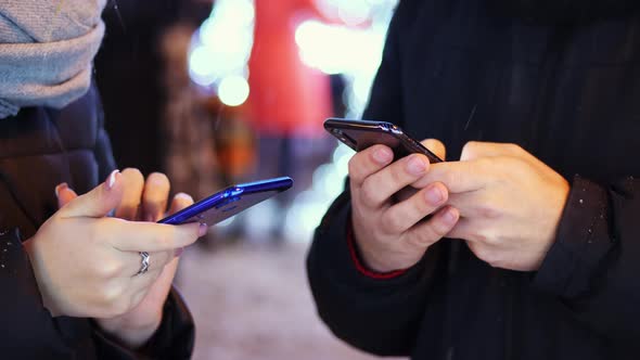 Closeup Hand of Man and Woman Uses Mobile App in the Snowy Evening