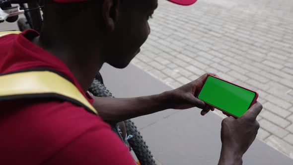 African Delivery Man Using Mobile Phone with Horizontal Green Mock Up Screen