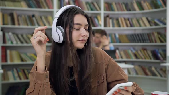 Woman with Straight Long Hair Relaxing Under Beautiful Songs on Headphones in the Reading Room