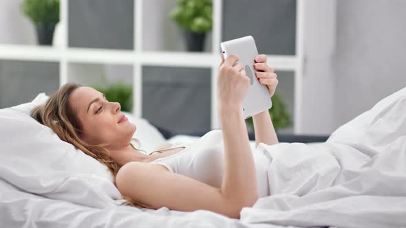 Pleasant Young Woman Lying on Bed Chatting Using Tablet Pc Enjoy Weekend