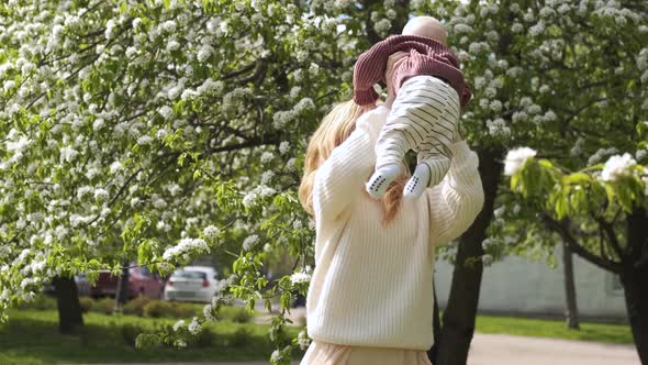 happy caucasian mom is spinning with her baby in a blooming garden
