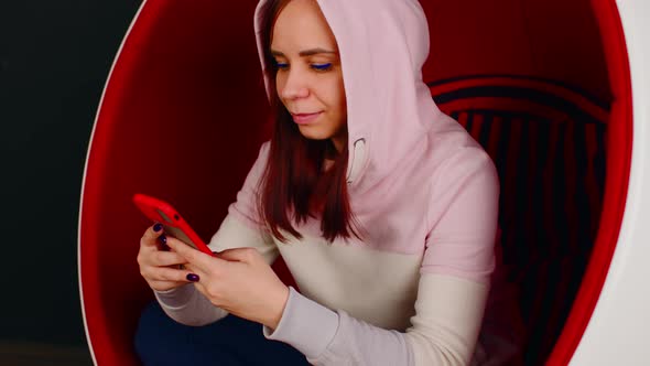 Young Woman with Mobile Phone Sitting in Ball Chair on Black Background