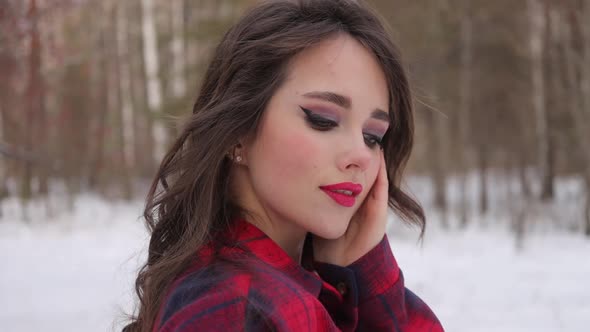 Young Woman with Wavy Hair Standing and Touching Face in Winter Forest