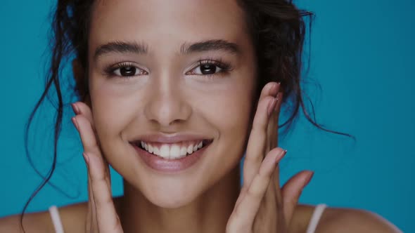 Close-up of Pretty Young Woman Massaging Cheeks and Laughing To Camera Isolated on Blue