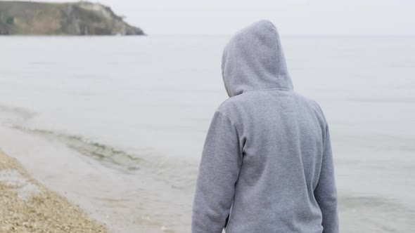Following Shot of an Unknown Person in a Hoodie Walking Along the Seashore