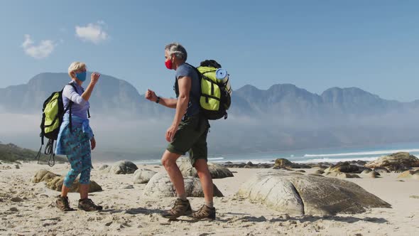 Senior hiker couple wearing face masks with backpacks greeting each other by touching elbows