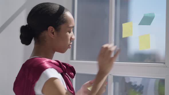 Side View of Charming Young Woman Sticking Adhesive Notes on Window Glass on Sunny Morning in Home