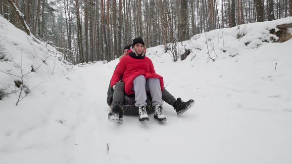 Happy Couple Having Fun and Riding Inner Tube in Winter Forest