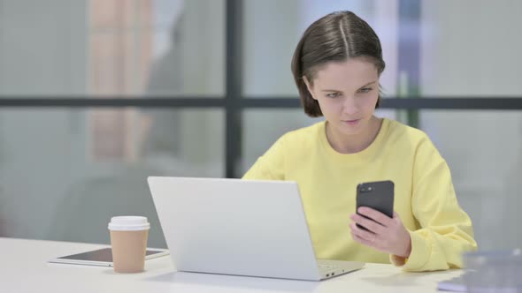 Young Woman Using Smartphone While Using Laptop in Office