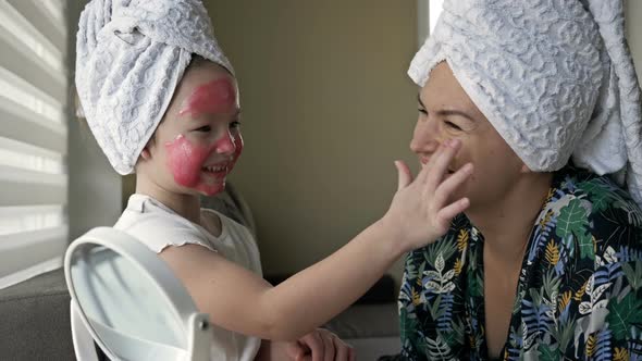 Little Girl with a Cosmetic Mask on Her Face Helps Her Mother To Make a Cosmetic Mask