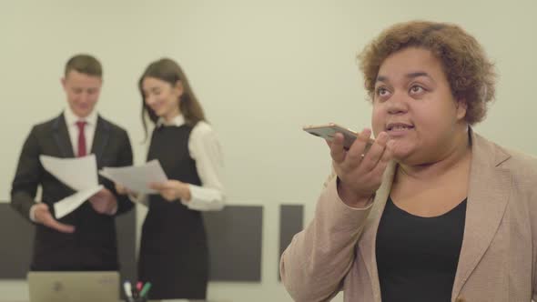 Portrait of Angry Woman in Formal Wear Speaks By Her Cellphone in the Foreground in the Office While