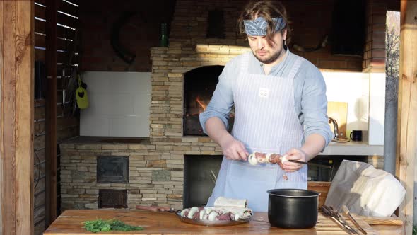 A Man in an Apron Strings Pieces of Meat on a Skewer and Makes a Kebab From It Near the Fireplace