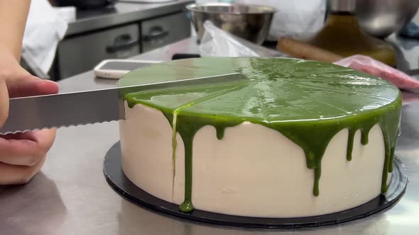 Rear shot of a professional french pastry chef using serrated knife to slice moist japanese matcha g