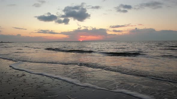 Static shot of waves hitting a beach, while the sunset turns to dusk