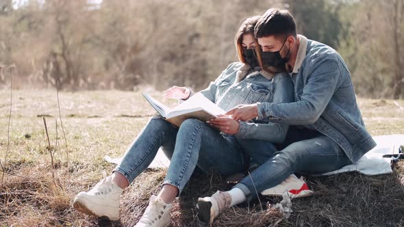 Attractive Young Man Is Hugging His Girlfriend Reading a Book in the Field