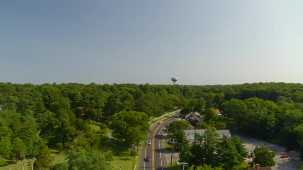 Flying Over a Main Road on a Suburban Small Town and Towards Dense Forest Trees