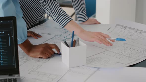 Close Up of Architects Doing Teamwork to Design Blueprints Plans for Building Model on Table