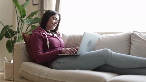 Young Adult Woman Relaxing on Sofa While Using Laptop Computer