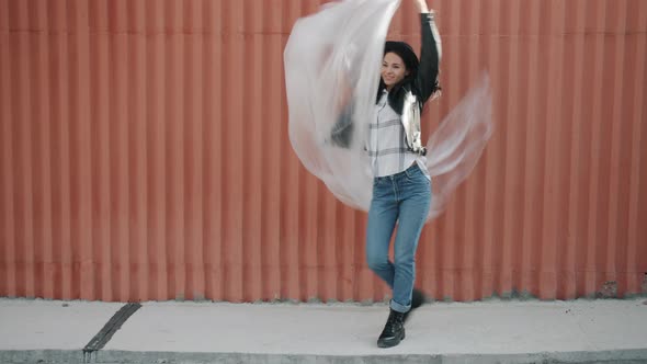 Portrait of Happy Girl Dancing with Polyethylene Sheet Waving in Air Having Fun Against Wall