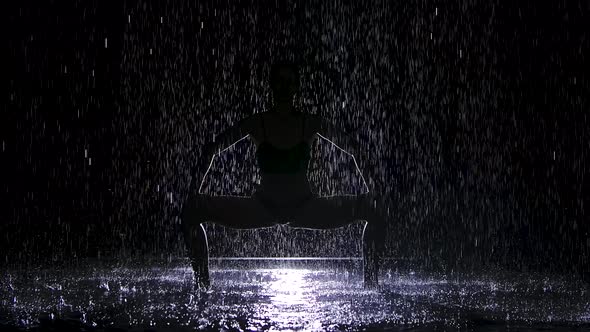 Doing Yoga Exercises in the Pouring Rain in a Dark Studio. A White Spotlight Illuminates the Surface