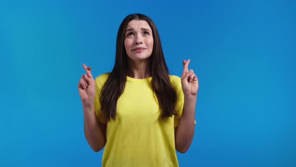 Cute Woman Praying with Crossed Fingers on Blue Background