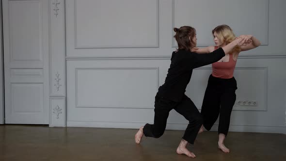 a Young Barefoot Couple is Dancing Against a Light Wall