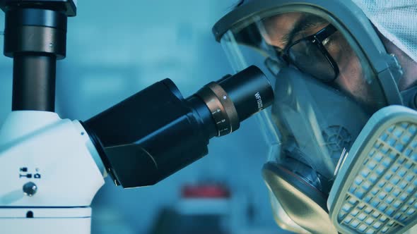 Scientist in a Hazmat Mask is Looking Into a Microscope