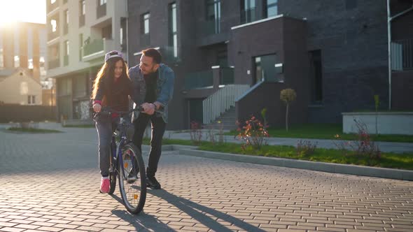 Dad Is Teaching Daughter How To Ride Bicycle at Sunset. Slow Motion