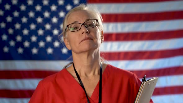 Portrait of a nurse walking from US flag to foreground and showing a smile and approval.